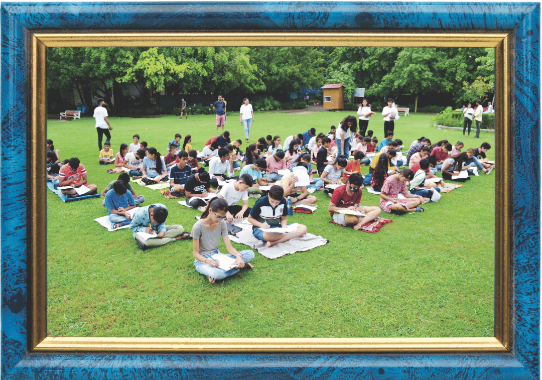 This is another framed image showing many students seated outdoors on grass, writing or taking an exam, similar to the previous one.